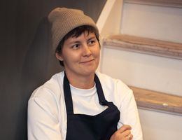 A person is sitting on a staircase wearing a cap and a work shirt. They look thoughtful and smile slightly.